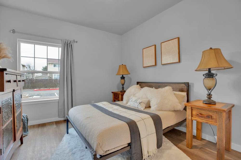 Primary bedroom with large window, wood-style flooring, and bedside tables, at Cleveland Crossings in Woodburn, Oregon