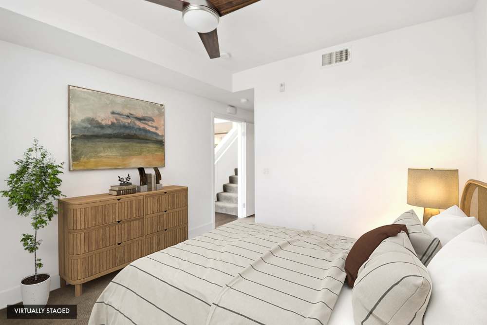 Virtually staged bedroom with wood dresser, ceiling fan, and modern furnishings at The Marke Apartment Homes in Santa Ana, California