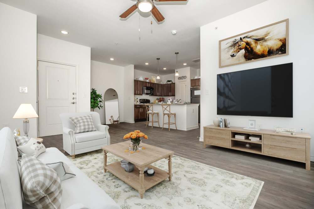 Bright open-concept living room with TV wall, coffee table, and kitchen, McKinney Falls Apartments in Austin, Texas