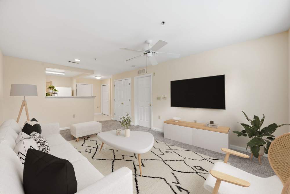 Bright living room with ceiling fan, television, and white couch at Waverly Gardens in Woodstock, Maryland