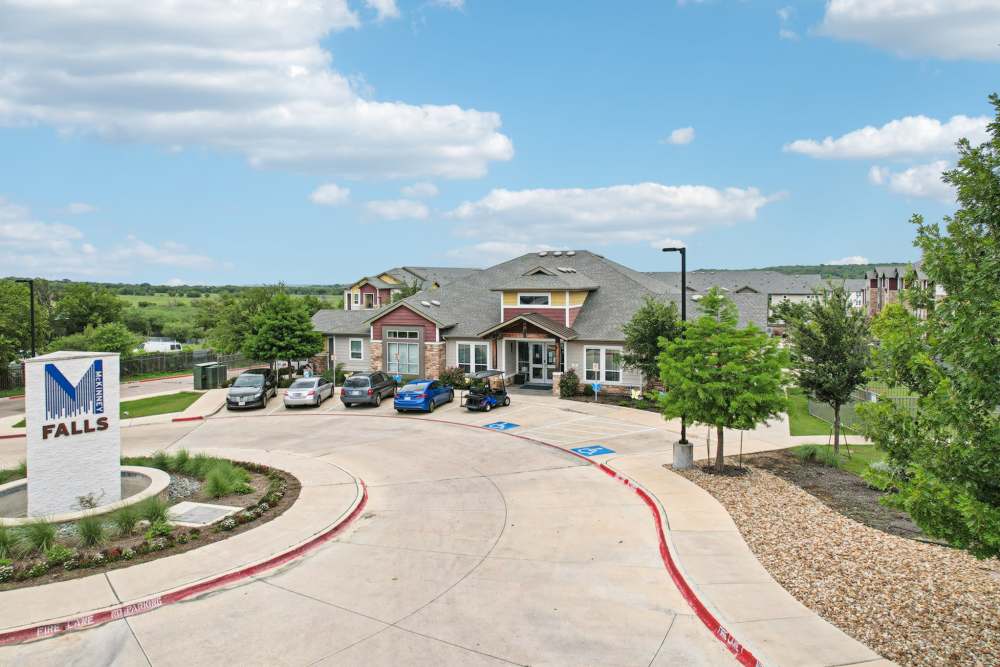 Community entrance with landscaped roundabout and residential homes at McKinney Falls Apartments in Austin, Texas