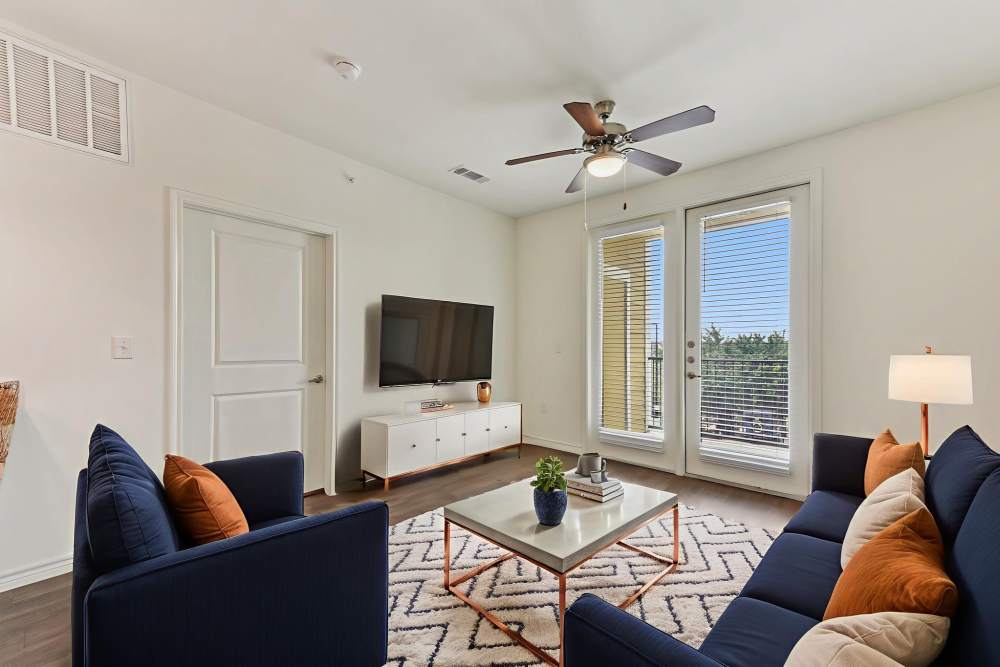 Modern living room with blue sofas, coffee table, area rug, and large windows at McKinney Falls Apartments in Austin, Texas