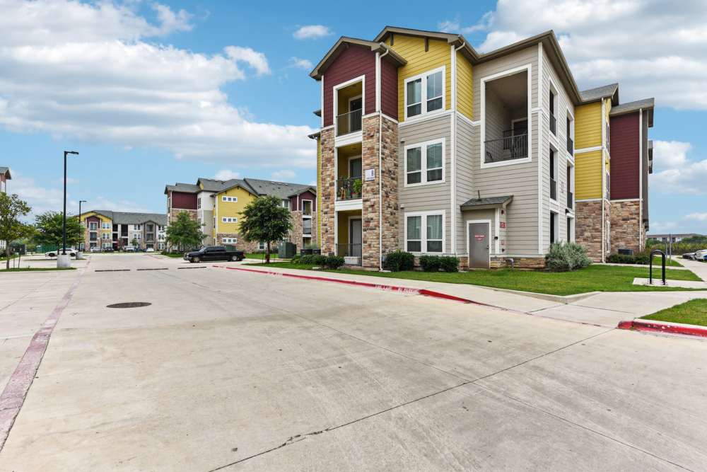 Exterior view of apartment-style community buildings and parking area at McKinney Falls Apartments in Austin, Texas