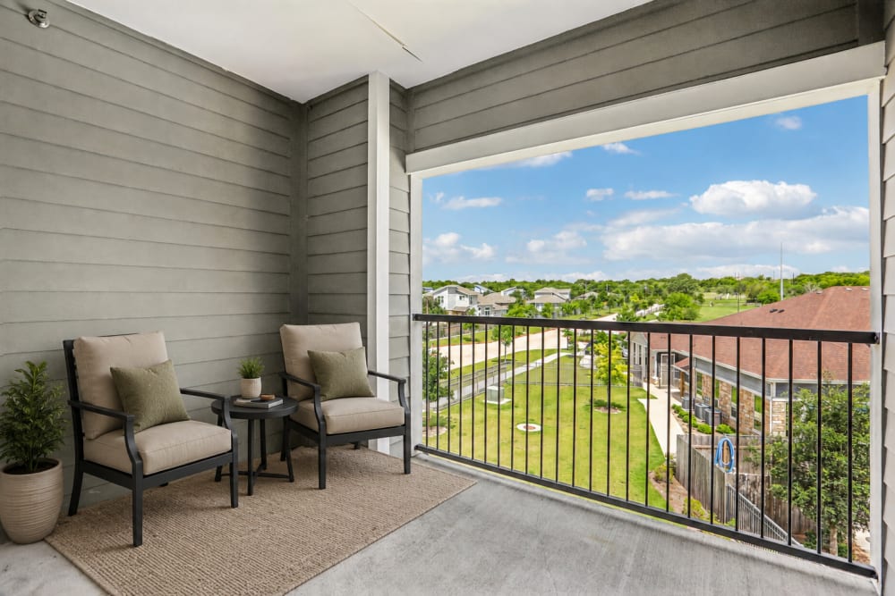Private covered balcony with outdoor seating and scenic community views at Limestone Ridge Apartments in Austin, Texas
