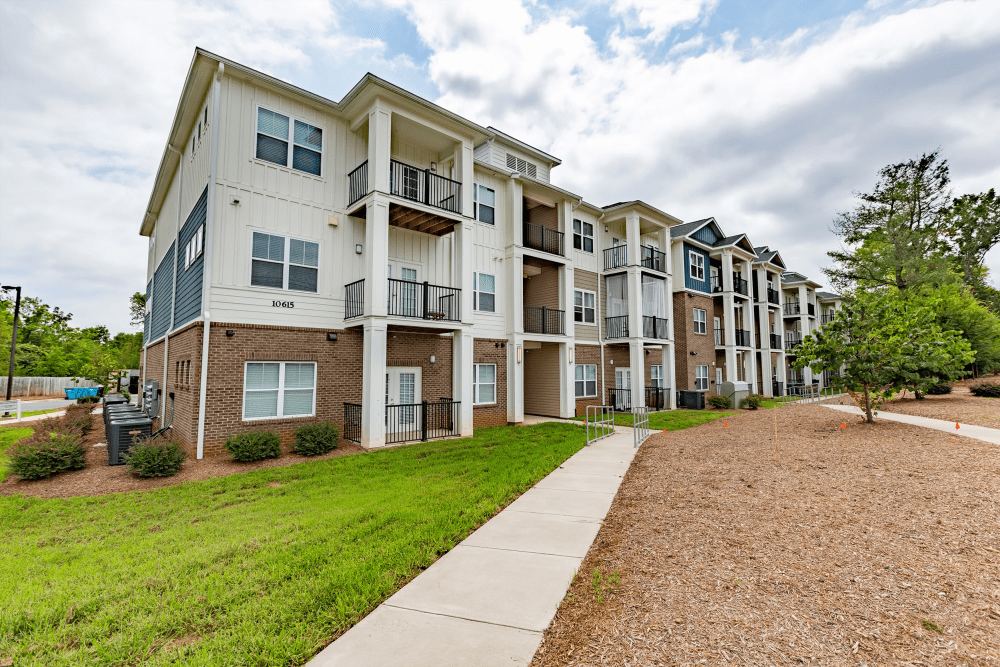 Apartment community building with landscaped lawn and walking path at Exchange at Steele Creek in Charlotte, North Carolina