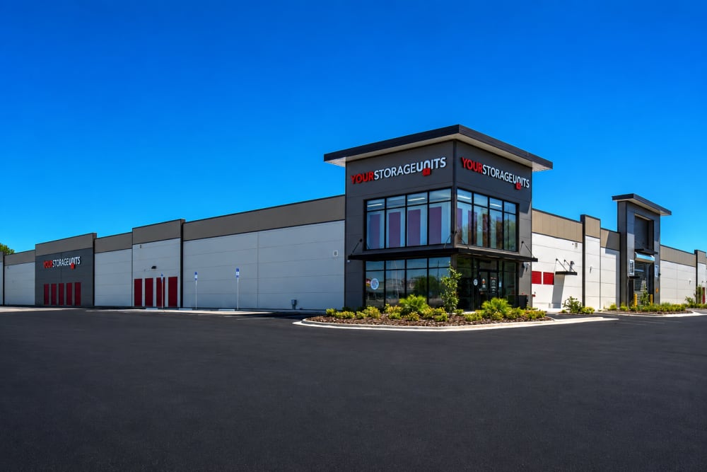 Exterior of YourStorageUnits facility with landscaped entrance and red unit doors at Your Storage Units Panama City in Panama City, Florida