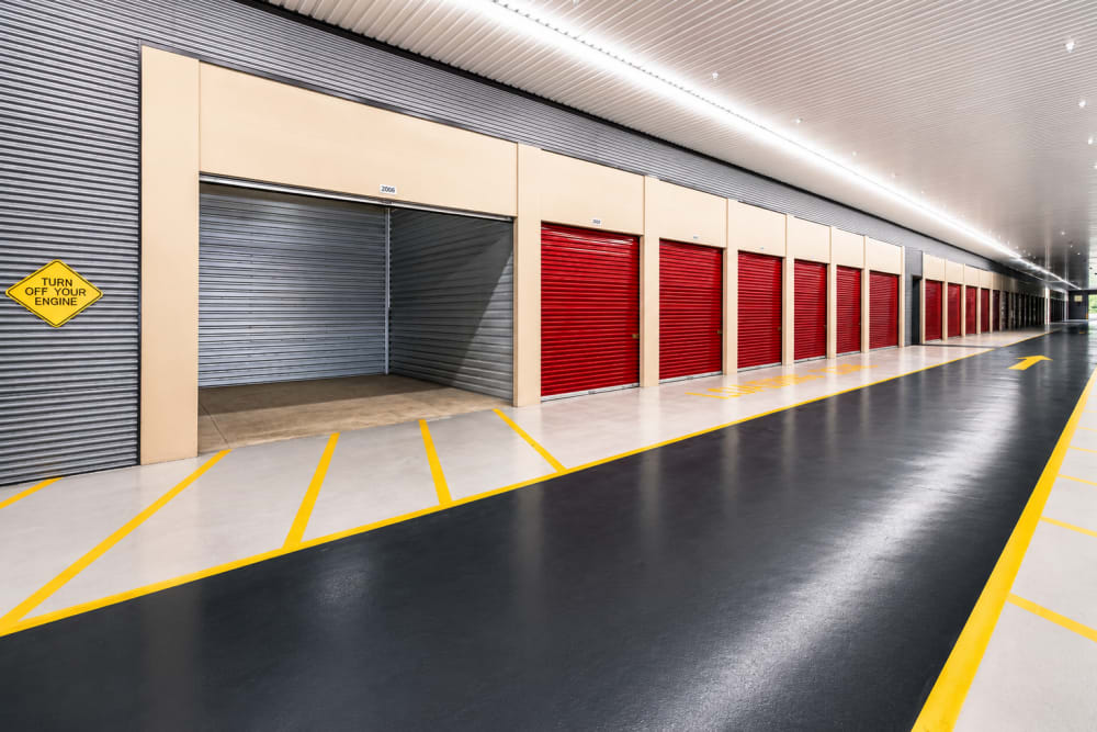 Storage unit hallway with red roll-up doors and one open unit at Your Storage Units Panama City in Panama City, Florida