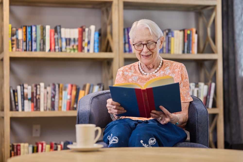 Senior woman reading a book in a cozy chair at Barclay House of Oakleaf Village in Lexington, South Carolina