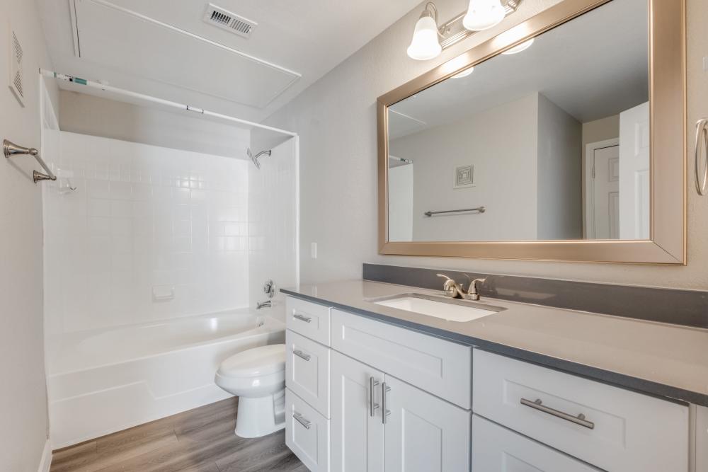 Modern bathroom with white tub, gray countertops, and large mirror, featuring wood-style flooring at Reeves and Wells in Dallas, Texas