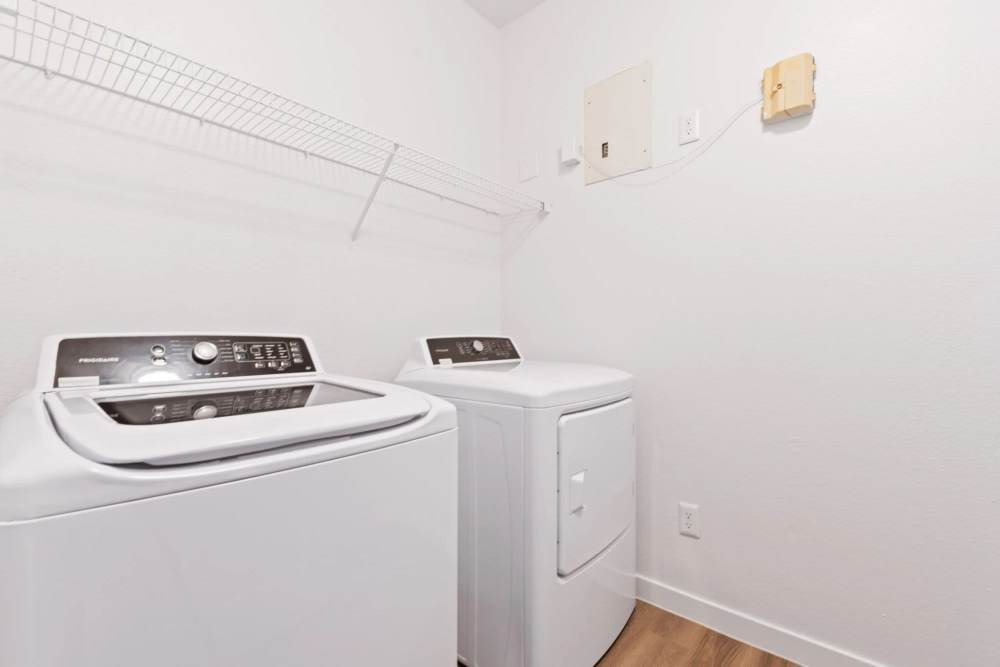 Bright laundry room featuring white washer and dryer with wood-style flooring and wire shelf above at Reeves and Wells in Dallas, Texas