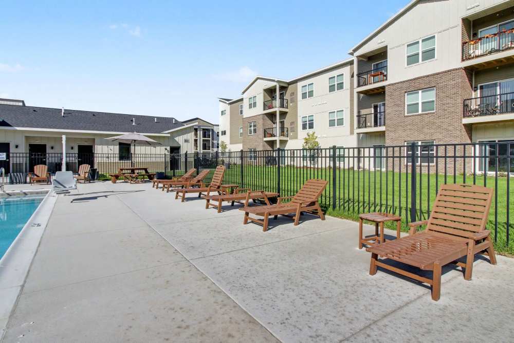 deck with a row of brown chaise lounge chairs, a picnic table with umbrella, and apartment buildings with brick and board-and-batten siding in the background at The Block at Petoskey in Petoskey, Michigan