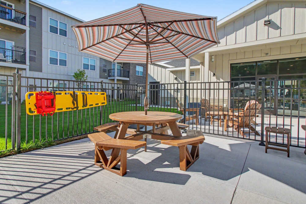 Poolside patio featuring a round picnic table with a striped umbrella, a wall-mounted spine board/rescue equipment on the fence, and additional lounge chairs nearby at The Block at Petoskey in Petoskey, Michigan