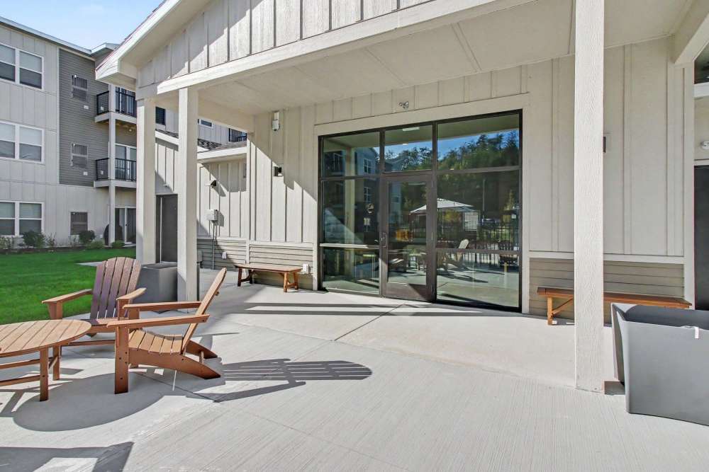 Covered outdoor patio with wooden Adirondack chairs, a bench, and glass double doors leading into a building, with a grassy lawn to the left at The Block at Petoskey in Petoskey, Michigan