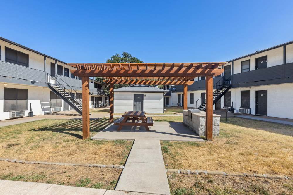 Courtyard with wooden pergola, picnic table and outdoor grill between buildings at Country Oaks in Weatherford, Texas