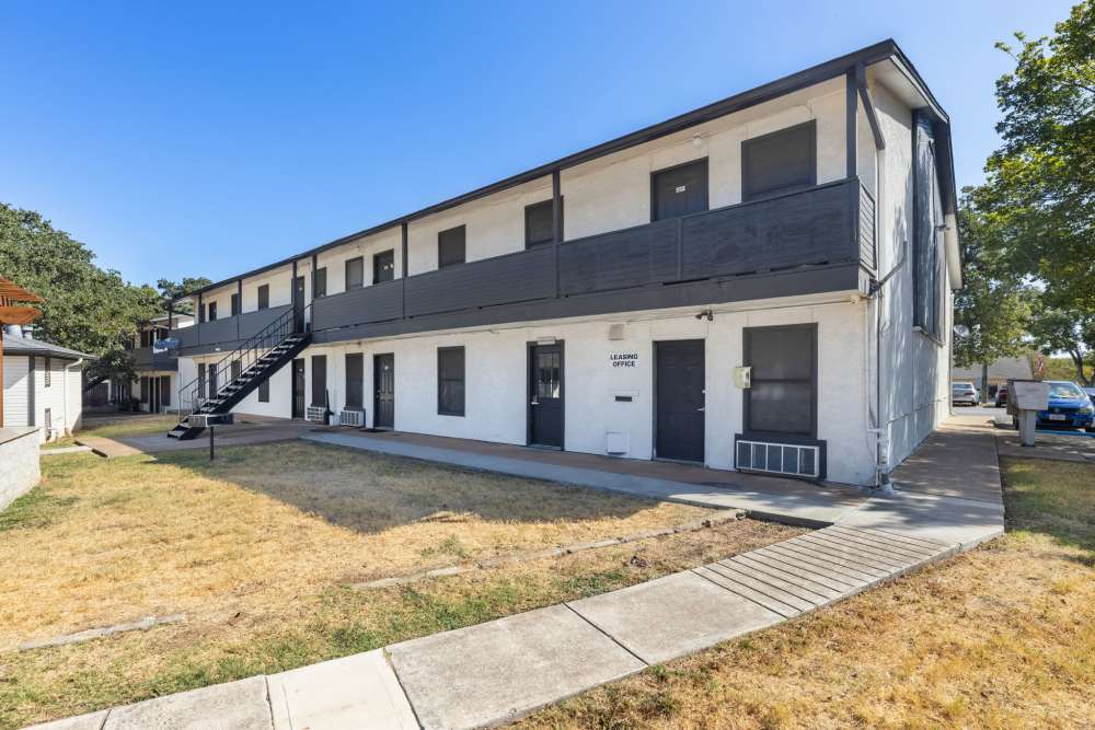 Exterior of white two-story apartment building with black balconies, stairs and leasing office at Country Oaks in Weatherford, Texas