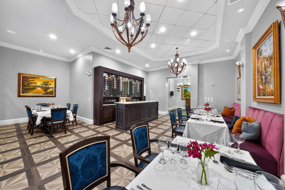 Private dining room with set tables, blue upholstered chairs, a wine display, and pink banquette seating at The Barclay at Vero Beach in Vero Beach, Florida