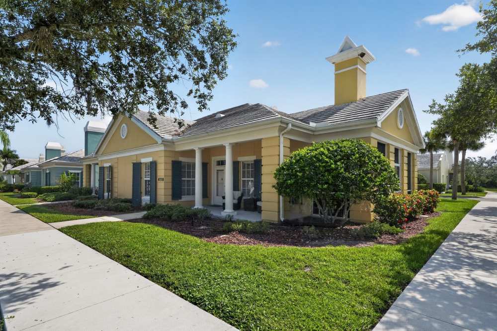Yellow single-story residence with white columns, blue shutters, a covered front porch, and landscaped lawn at The Barclay at Vero Beach in Vero Beach, Florida