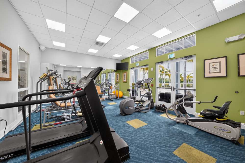 Fitness room with treadmills, a NuStep recumbent stepper, strength machines, and French doors to the pool at The Barclay at Vero Beach in Vero Beach, Florida