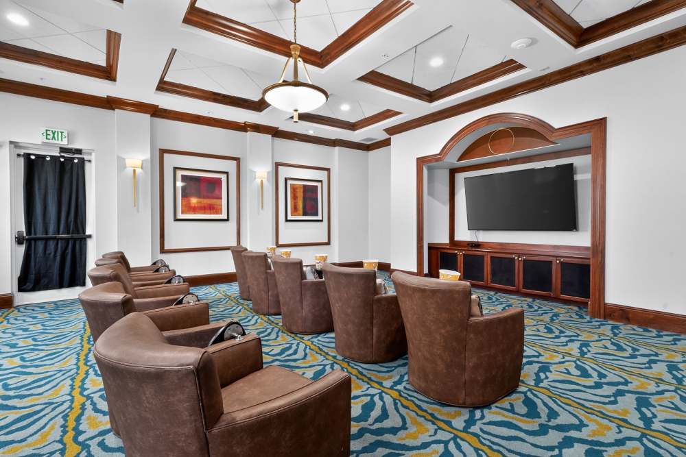 Private movie theater room with brown leather swivel chairs, a wall-mounted TV, and coffered wood-trimmed ceiling at The Barclay at Vero Beach in Vero Beach, Florida