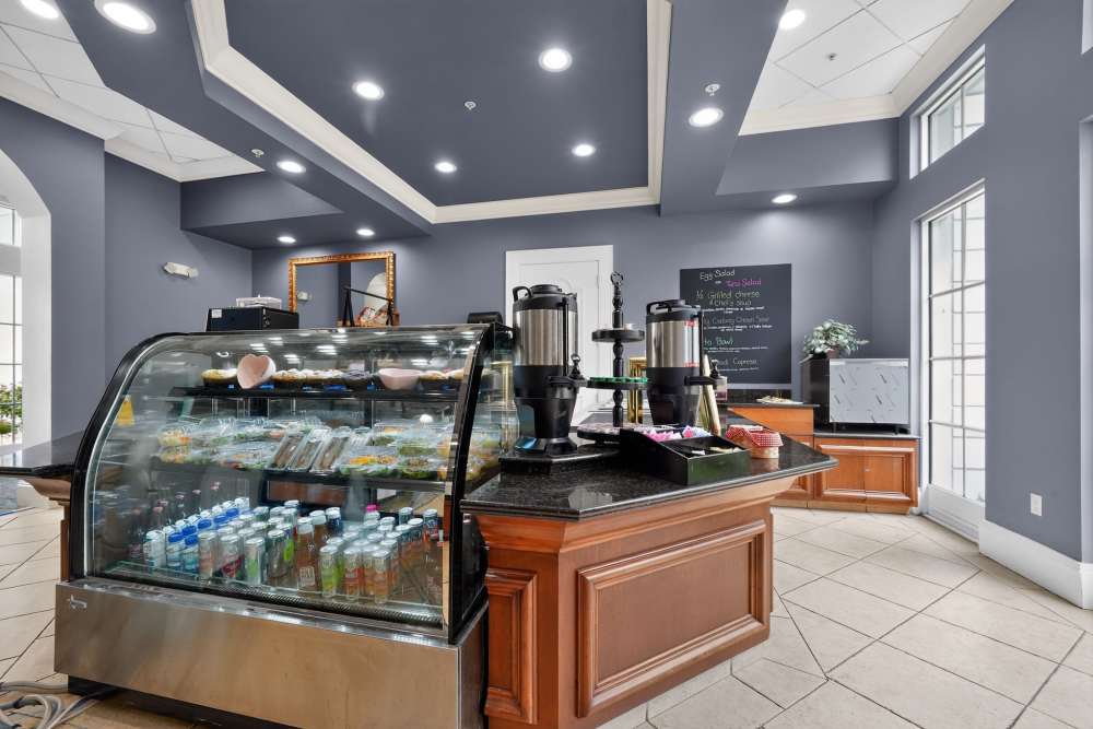 Café with a refrigerated display case of sandwiches and drinks, coffee dispensers, and a chalkboard menu at The Barclay at Vero Beach in Vero Beach, Florida