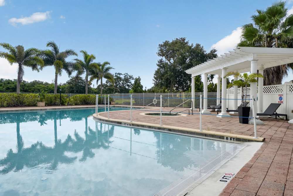Resort-style pool with a white pergola, lounge chairs, hot tub, and surrounding palm trees at The Barclay at Vero Beach in Vero Beach, Florida