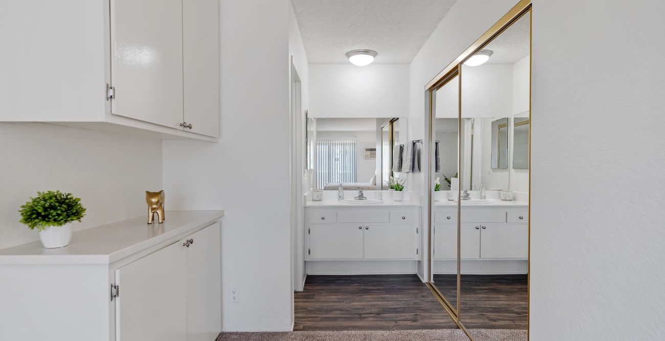 Walkway from the bedroom to the bathroom at the one bedroom townhome style apartment with wall cabinetry, large closet with mirrored doors, and a vanity with more storage at Vista Pointe II in Studio City, California