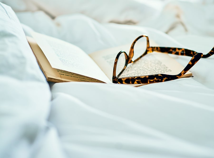 A book and some reading glasses sitting on a bedcover at The Meridian at Boca Raton in Boca Raton, Florida