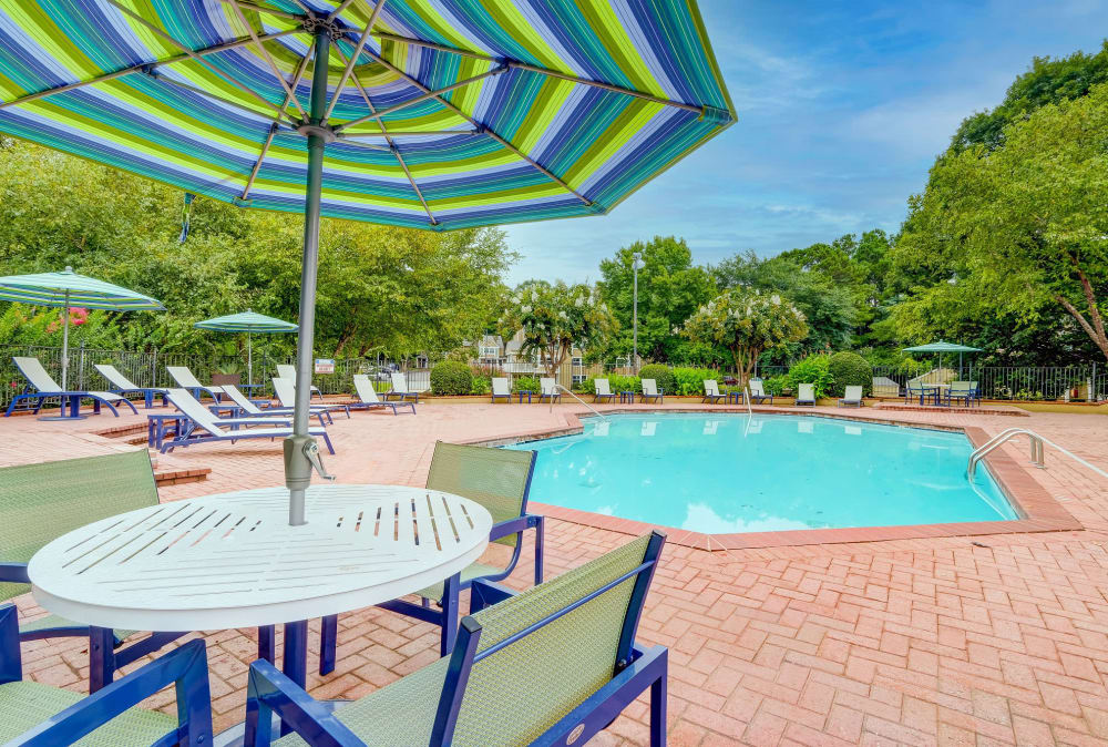 Patio tables, chairs, and umbrellas around pool at Grove at Stonebrook Apartments & Townhomes in Norcross, Georgia