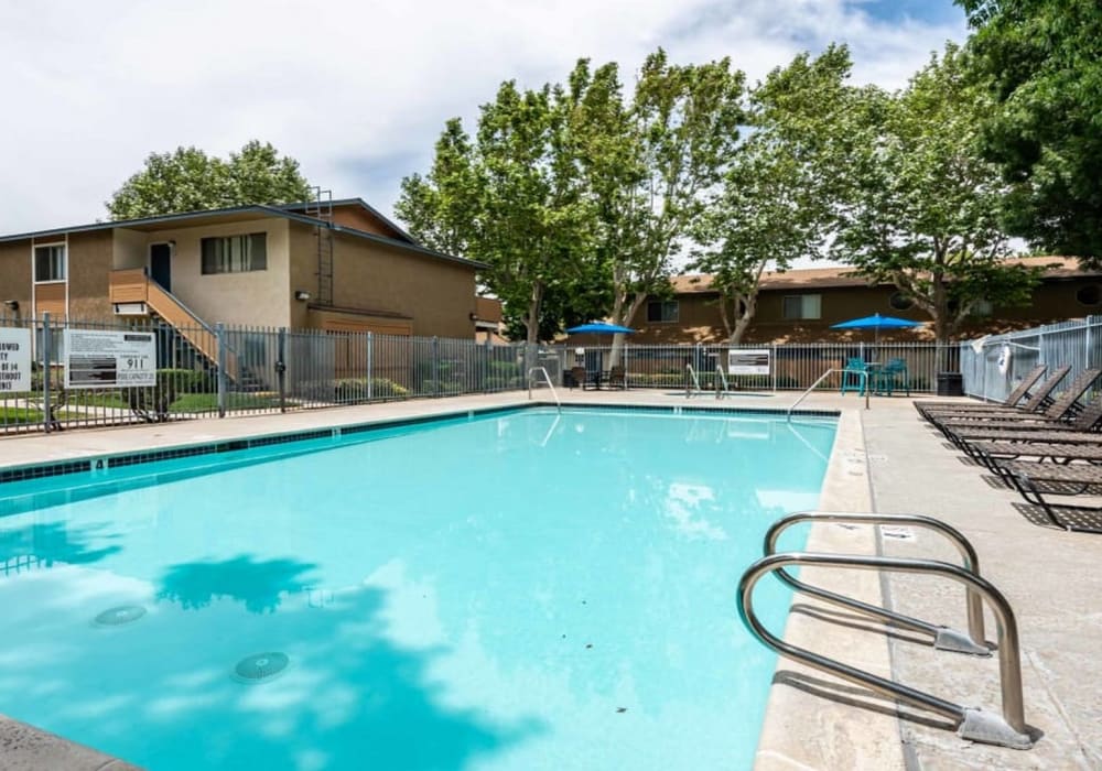 Community pool with outdoor lounge chairs at Sienna Heights Apartments apartment homes in Lancaster, California