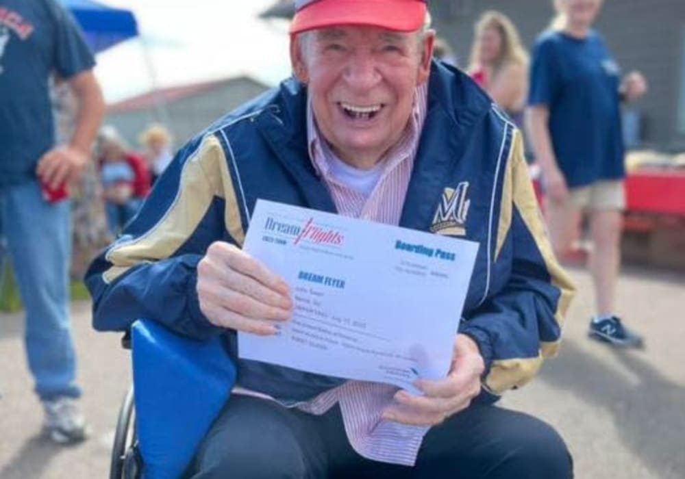 Smiling resident holds his certificate after enjoying a flight in a World War ll biplane courtesy of Dream Flights in Bell Tower Residence Assisted Living in Merrill, Wisconsin