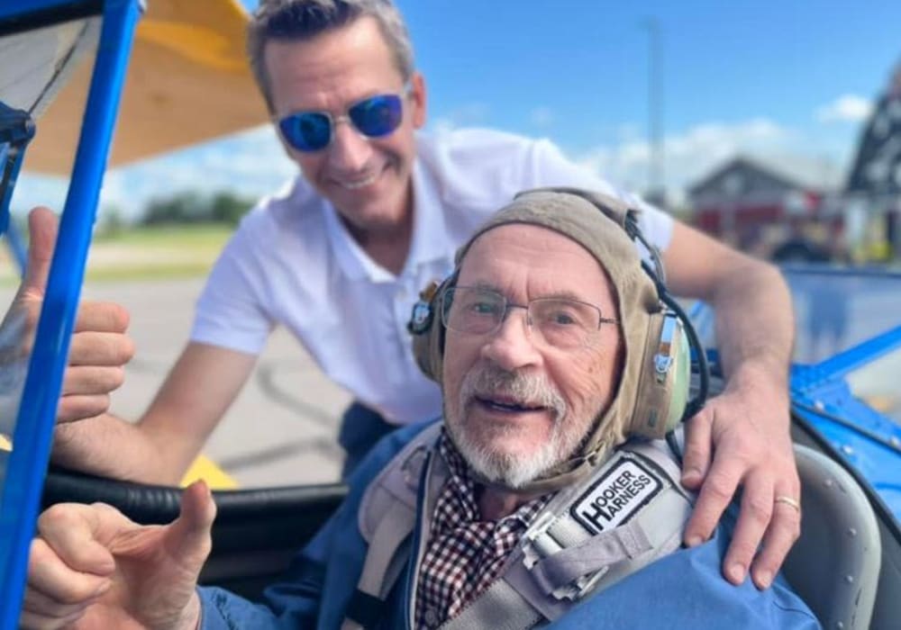 Resident sitting in a WWII open-cockpit biplane poses with a Dream Flights team member just before taking a free flight in Bell Tower Residence Assisted Living in Merrill, Wisconsin