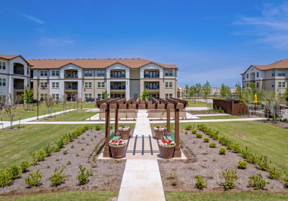 A paved walkway leading to outdoor benches surrounded by grass at Mariposa at Clear Creek in Webster, Texas