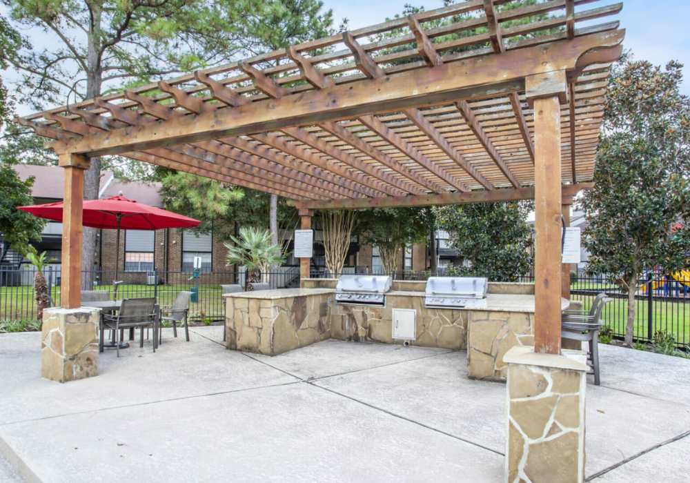 A wooden pergola covers an outdoor grilling and dining area with a stone countertop and built-in-grills at Rayfords Edge Apartments in Spring, Texas