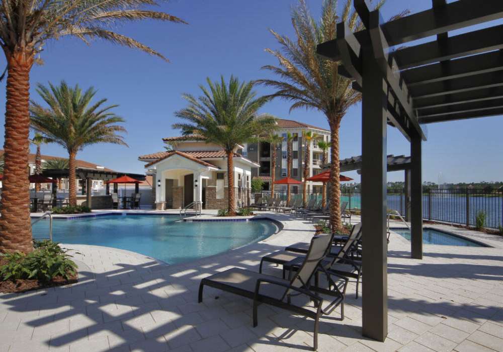 Resort-style pool with palm trees and scenic waterfront views at Messina Luxury Apartments in New Smyrna Beach, Florida
