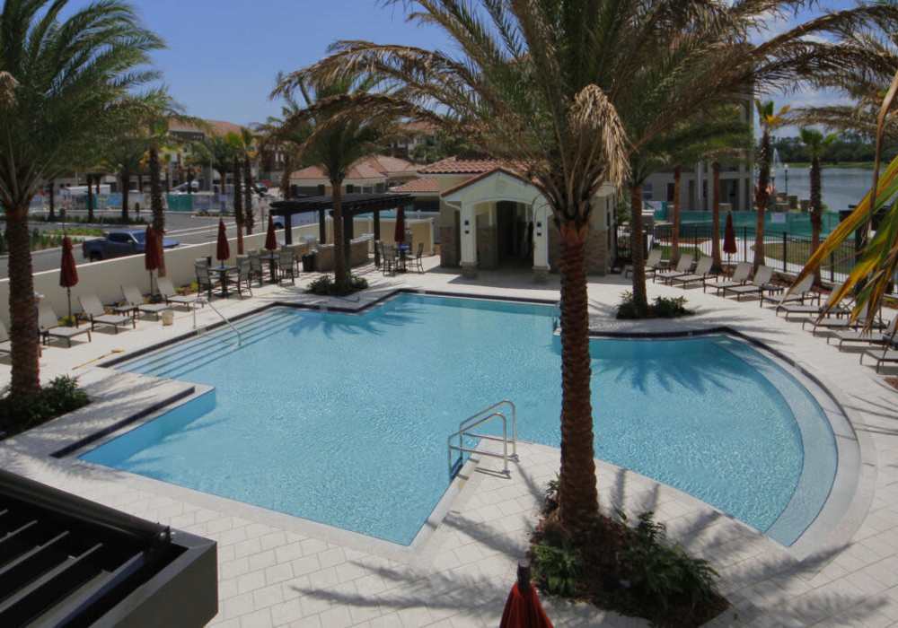 Sparkling pool surrounded by palm trees and lounge chairs at Messina Luxury Apartments in New Smyrna Beach, Florida