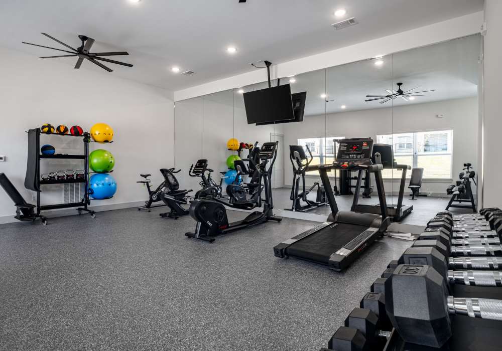 Modern gym with exercise equipment and mirrors at Terrace at Southern Oaks in Dallas, Texas