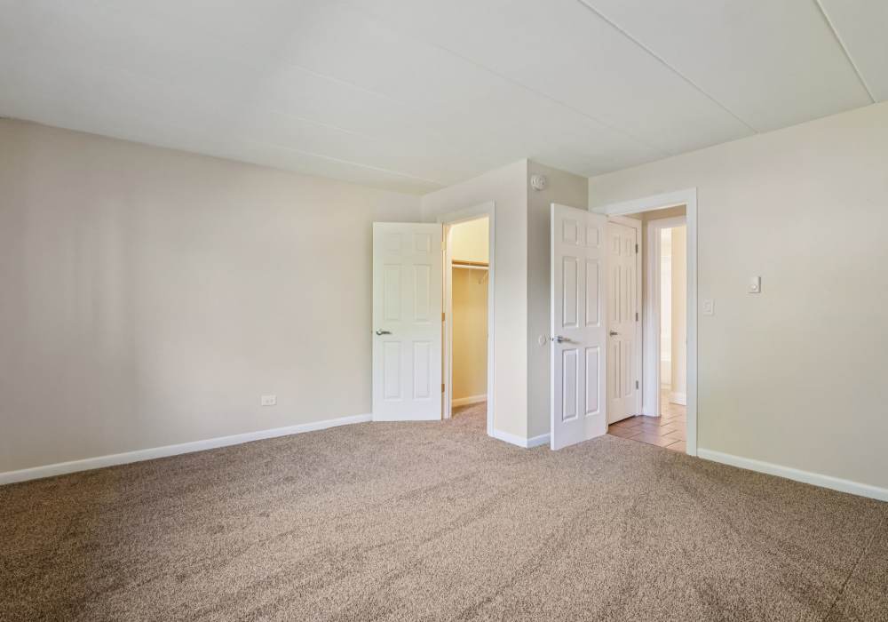 Carpeted bedroom with open closet and doors at Regents Park Apartments in Bensenville, Illinois