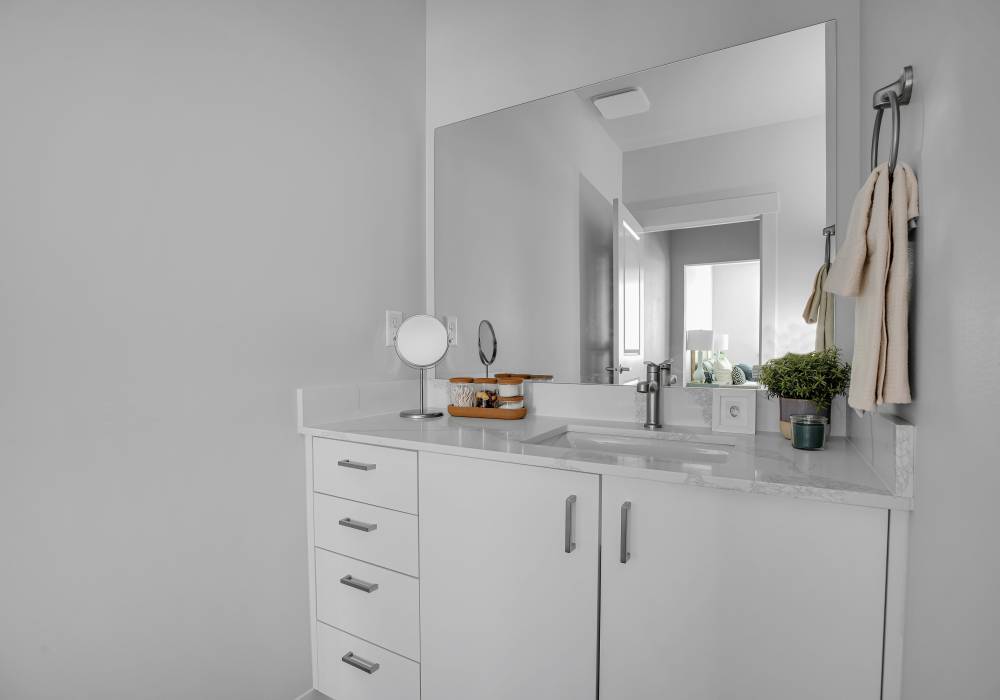 New bathroom with white cabinetry, marble countertop, large mirror, and decorative plants at Tilian Point in Woodburn, Oregon