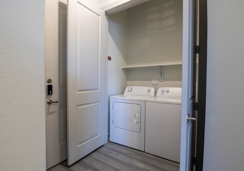 Compact in-unit laundry closet featuring a white top-load washing machine and matching front-load dryer at Charleston at Fannin Station in Houston, Texas