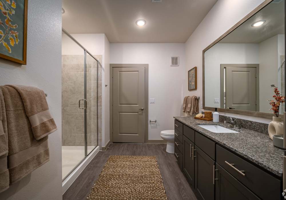 Spacious apartment bathroom featuring a long granite double vanity with dark wood cabinetry at Charleston at Fannin Station in Houston, Texas