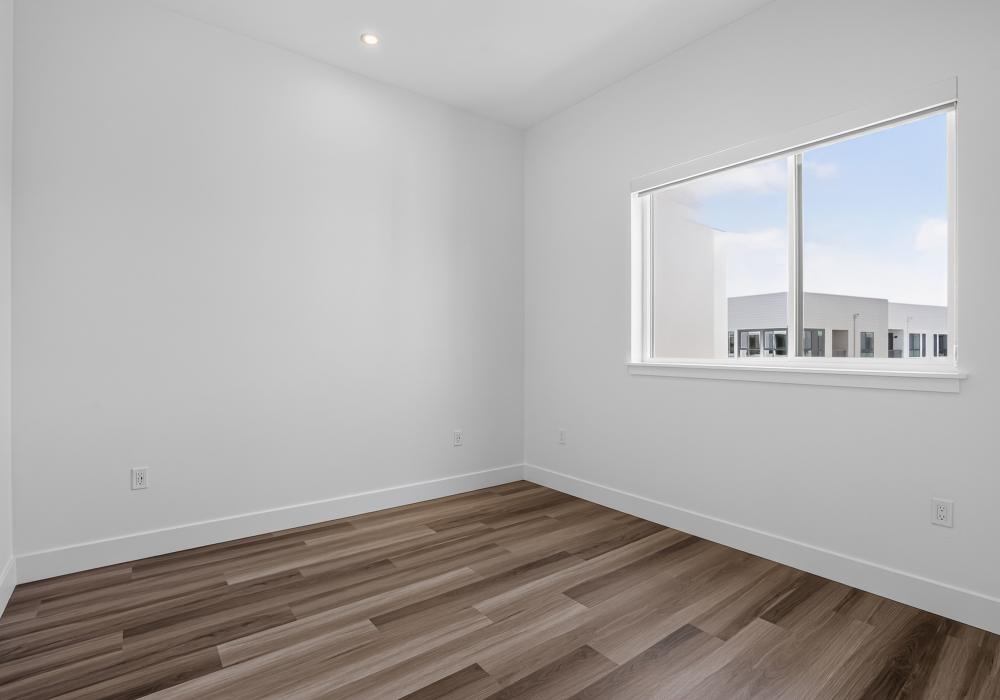 Empty bedroom corner with wide window and wood-style plank flooring at The Colton in Redwood City, California