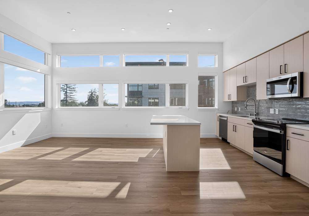 Sunlit kitchen with wall of windows, quartz island and light cabinets at The Colton in Redwood City, California