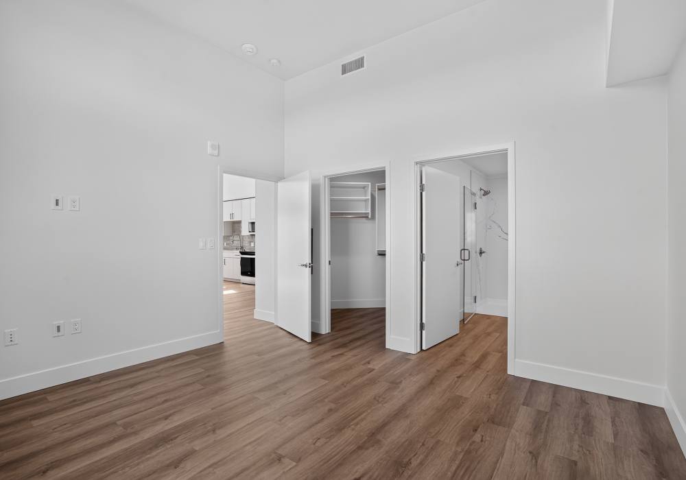 Bedroom with doors open to walk-in closet, glass shower and kitchen at The Colton in Redwood City, California