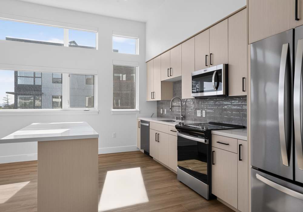 Galley kitchen with light cabinets, gray backsplash and island by windows at The Colton in Redwood City, California