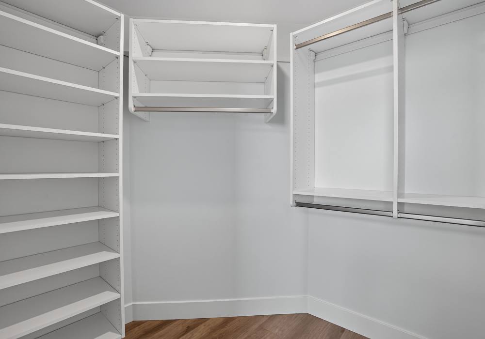 Walk-in closet with white shelving, hanging rods and wood-style flooring at The Colton in Redwood City, California