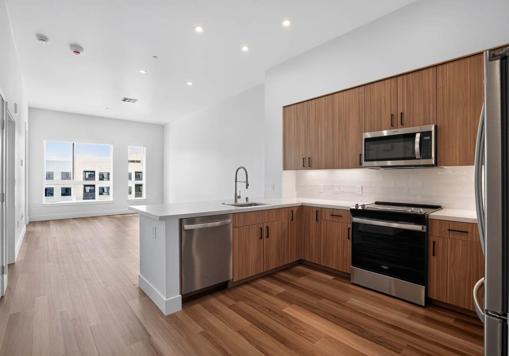 Kitchen with wood cabinets, breakfast bar and open living area with windows at The Colton in Redwood City, California