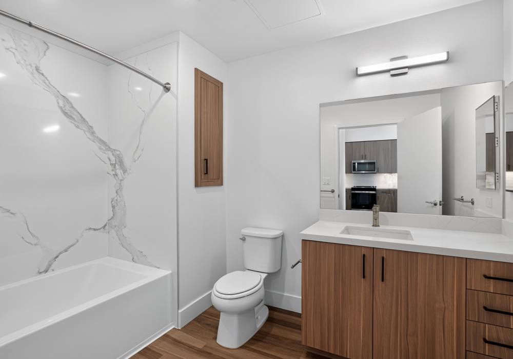 Bathroom with tub, marble surround, toilet and wood vanity with mirror at The Colton in Redwood City, California
