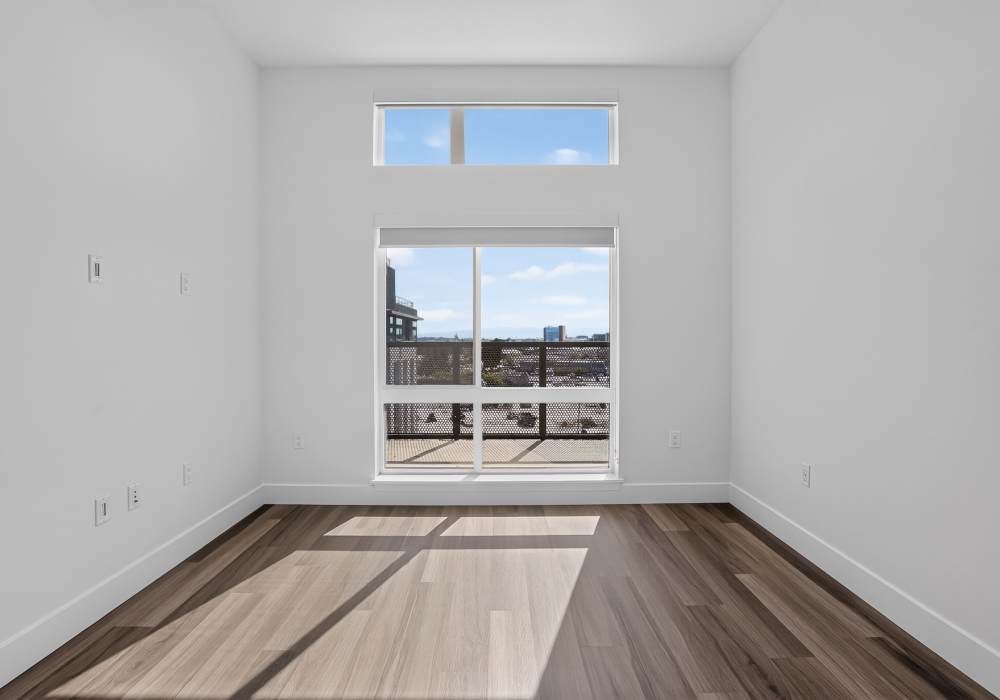 Empty bedroom with tall window, balcony view and plank flooring at The Colton in Redwood City, California