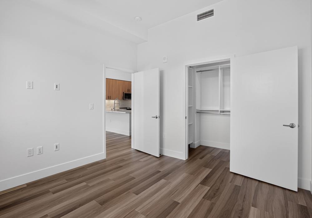 Empty bedroom with open closet doors and view into the kitchen at The Colton in Redwood City, California