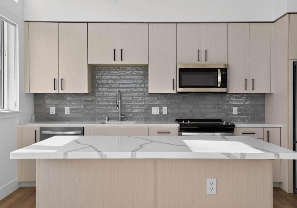 Kitchen with light cabinets, gray tile backsplash and quartz island at The Colton in Redwood City, California